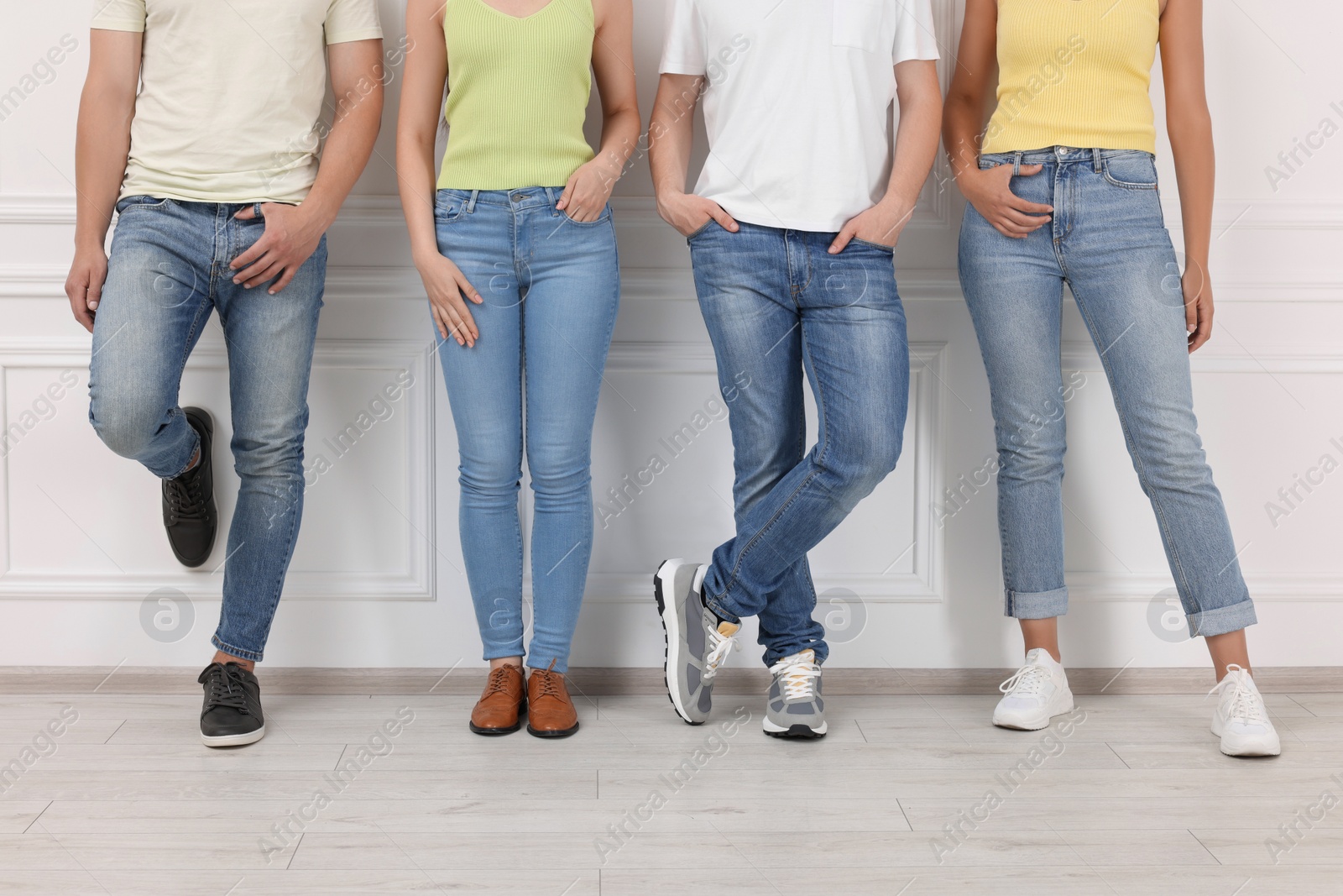 Photo of Group of people in stylish jeans near white wall indoors, closeup