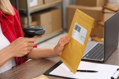 Photo of Seller with scanner reading parcel barcode at table in office, closeup. Online store