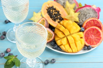 Photo of Delicious exotic fruits and wine on light blue wooden table