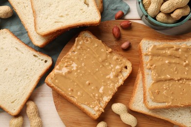 Photo of Delicious toasts with peanut butter and nuts on light wooden table, flat lay