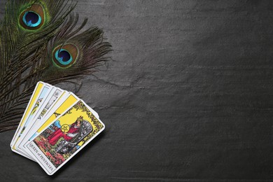 Photo of Tarot cards and peacock feathers on black table, flat lay. Space for text