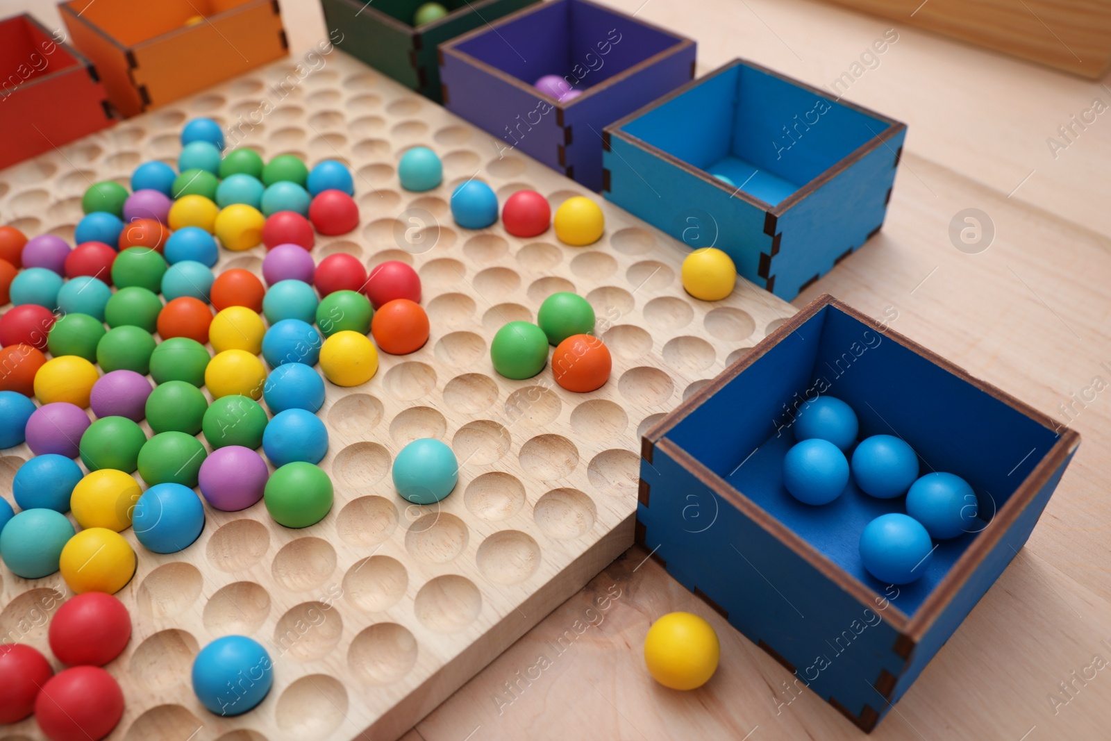Photo of Wooden sorting board and boxes with colorful balls on table, closeup. Montessori toy