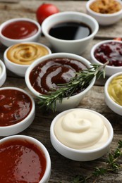 Photo of Different tasty sauces in bowls, rosemary and thyme on wooden table, closeup