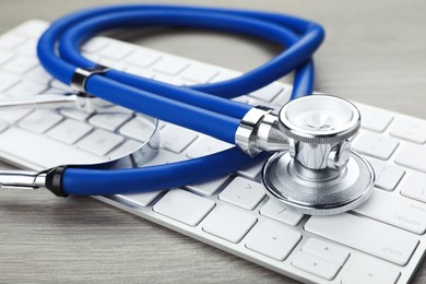 Photo of Computer keyboard with stethoscope on wooden table, closeup