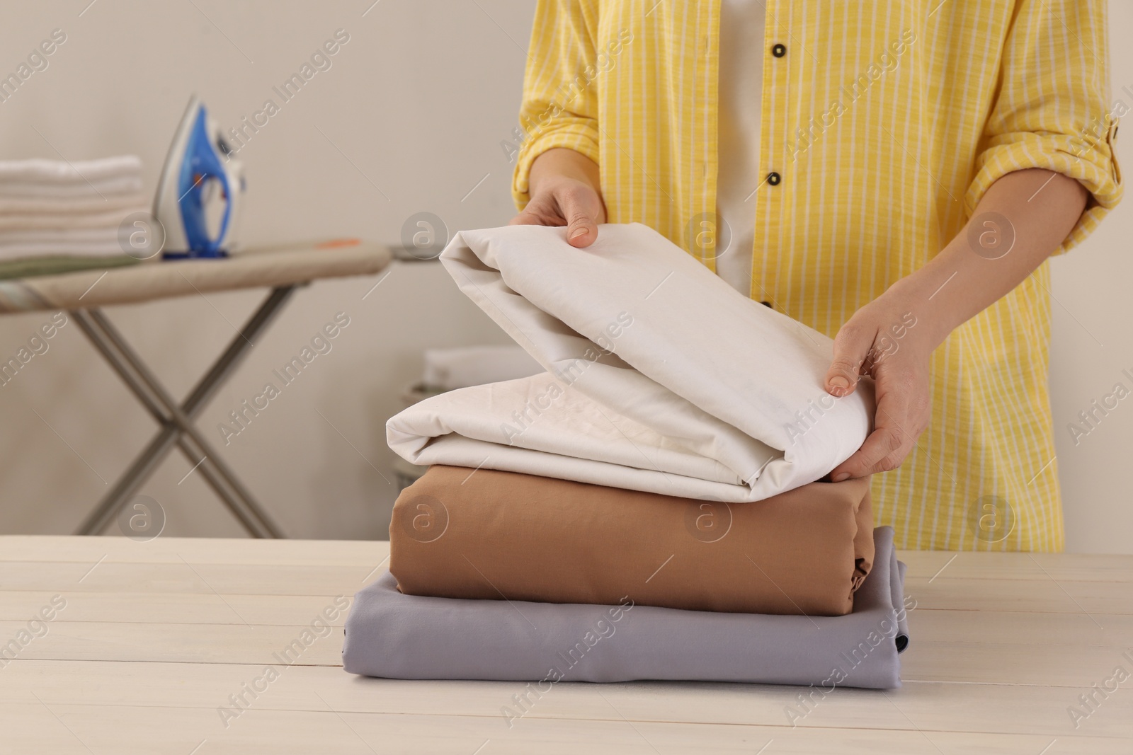 Photo of Woman with clean bed linens at white wooden table in laundry room, closeup