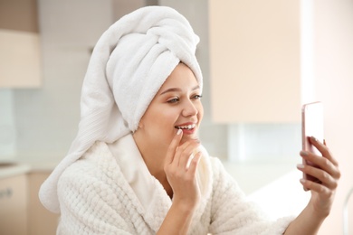 Photo of Beautiful woman with hair wrapped in towel taking selfie at home
