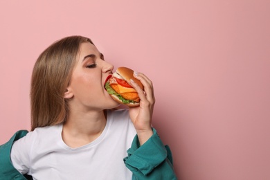 Pretty woman eating tasty burger on color background. Space for text