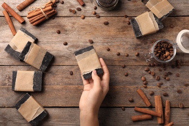 Woman holding handmade soap bar over table with ingredients, top view