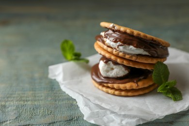 Photo of Delicious marshmallow sandwiches with crackers, mint and chocolate on light blue wooden table, closeup. Space for text