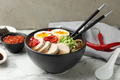 Delicious ramen in bowl on white marble table, closeup. Noodle soup