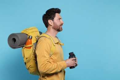 Photo of Man with backpack and binoculars on light blue background, space for text. Active tourism