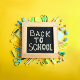 Photo of Chalkboard with phrase "BACK TO SCHOOL" and different stationery on yellow background, flat lay