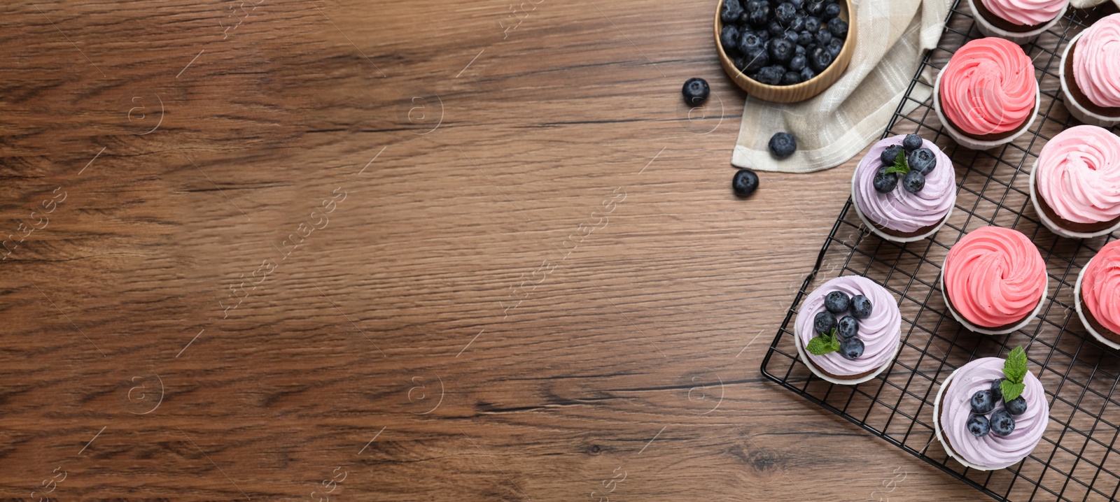 Image of Sweet cupcakes with fresh blueberries on wooden table, flat lay with space for text. Banner design