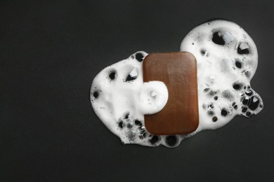 Photo of Soap bar and foam on black background, top view. Space for text