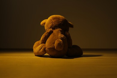 Photo of Cute lonely teddy bear on floor in dark room