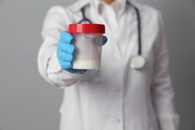 Photo of Doctor holding container with sperm on grey background, closeup