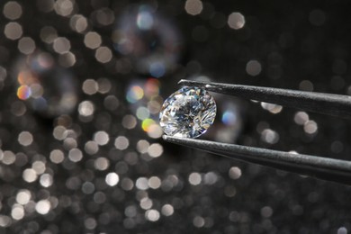Photo of Tweezers with beautiful diamond on dark shiny background, closeup