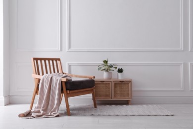 Photo of Comfortable wooden armchair with blanket and beautiful plants near white wall indoors