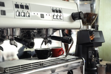 Photo of Modern coffee machine with cups in cafe, closeup