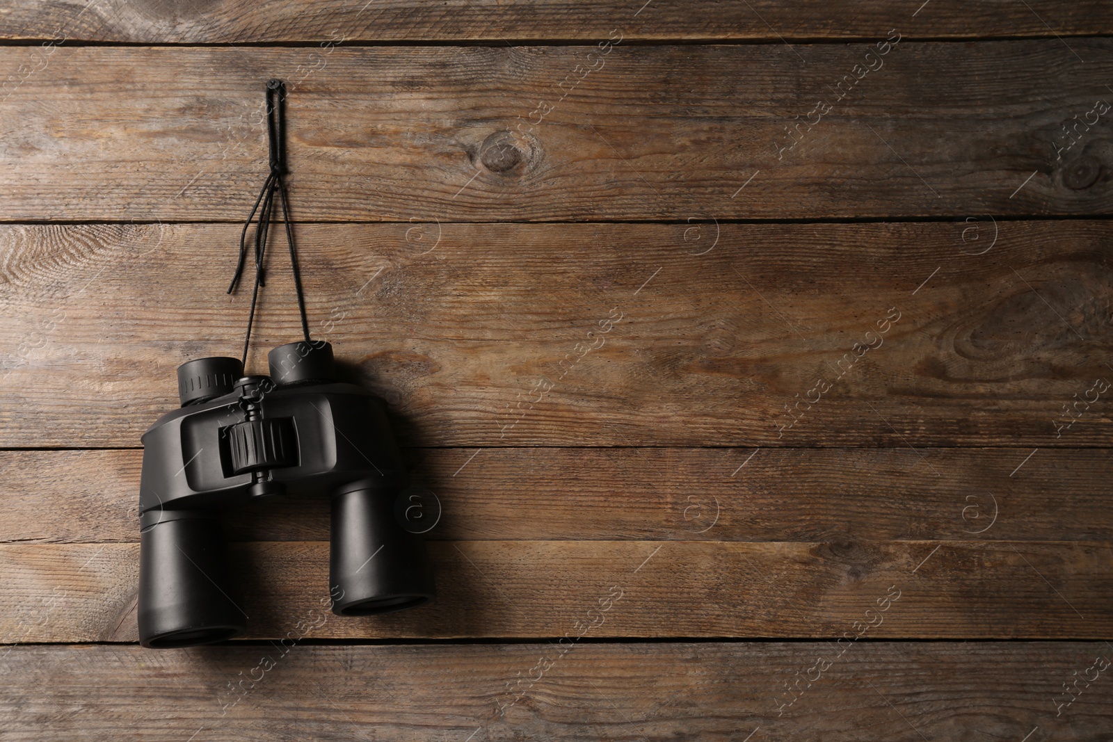 Photo of Modern binoculars hanging on wooden wall, space for text