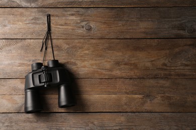 Photo of Modern binoculars hanging on wooden wall, space for text