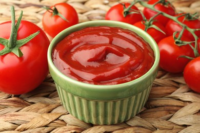 Photo of Bowl of tasty ketchup and tomatoes on wicker mat, closeup
