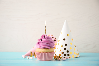 Photo of Delicious birthday cupcake with burning candle on light blue wooden table