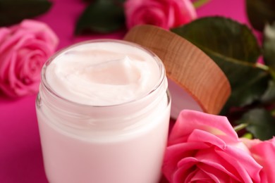 Glass jar of face cream and roses on pink background, closeup