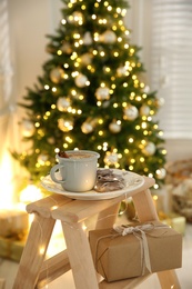 Photo of Tasty hot drink and cookies in room with Christmas tree