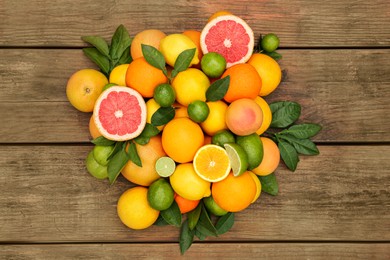 Photo of Different citrus fruits with green leaves on wooden table, flat lay