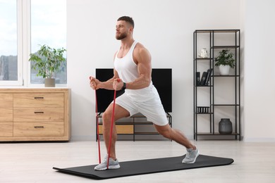 Photo of Athletic man doing exercise with elastic resistance band on mat at home
