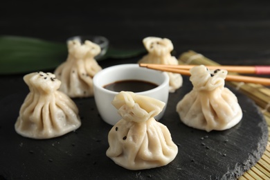 Photo of Slate plate with tasty baozi dumplings, chopsticks and soy sauce on table