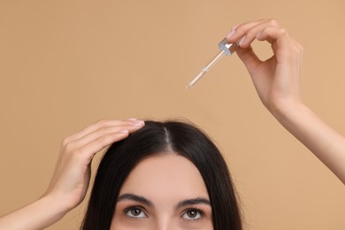 Photo of Woman applying hair serum on beige background, closeup. Cosmetic product