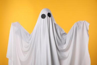 Photo of Creepy ghost. Person covered with white sheet on yellow background