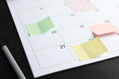 Photo of Timetable. Planner with sticky notes and pen on black wooden table, closeup