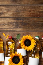 Photo of Bottles of sunflower cooking oil and beautiful flowers on wooden table, flat lay. Space for text
