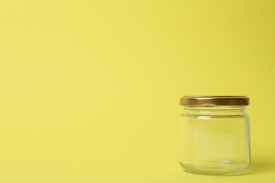 Closed empty glass jar on light yellow background, space for text