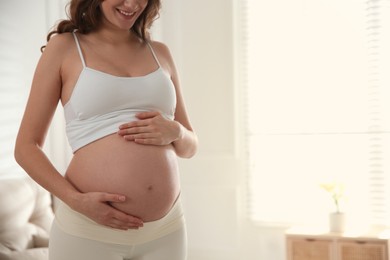 Photo of Pregnant woman touching her belly indoors, closeup