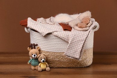 Laundry basket with baby clothes and soft toys on wooden table