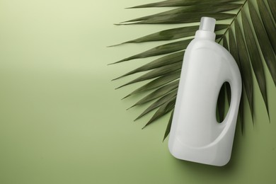 Photo of Bottle of fabric softener and palm leaf on light green background, flat lay. Space for text