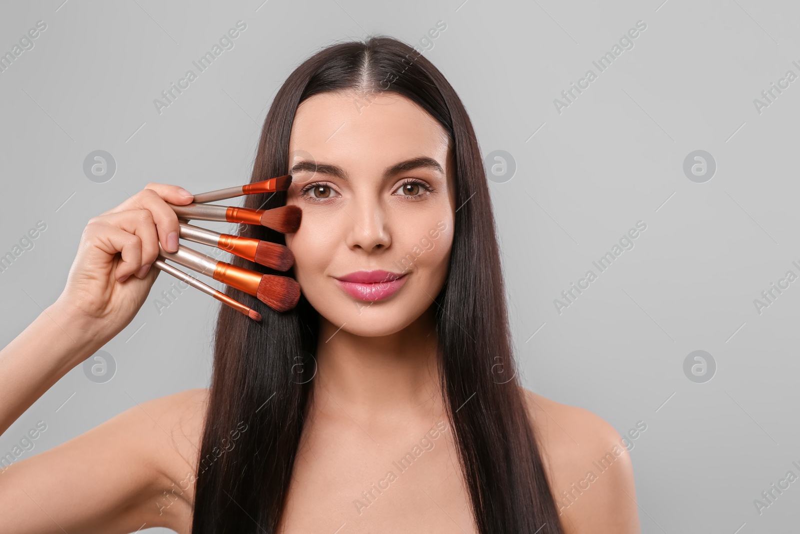 Photo of Beautiful woman with different makeup brushes on light grey background