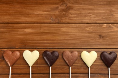 Photo of Different chocolate heart shaped lollipops on wooden table, flat lay. Space for text