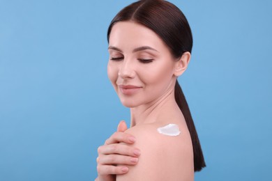 Photo of Beautiful woman with smear of body cream on her shoulder against light blue background