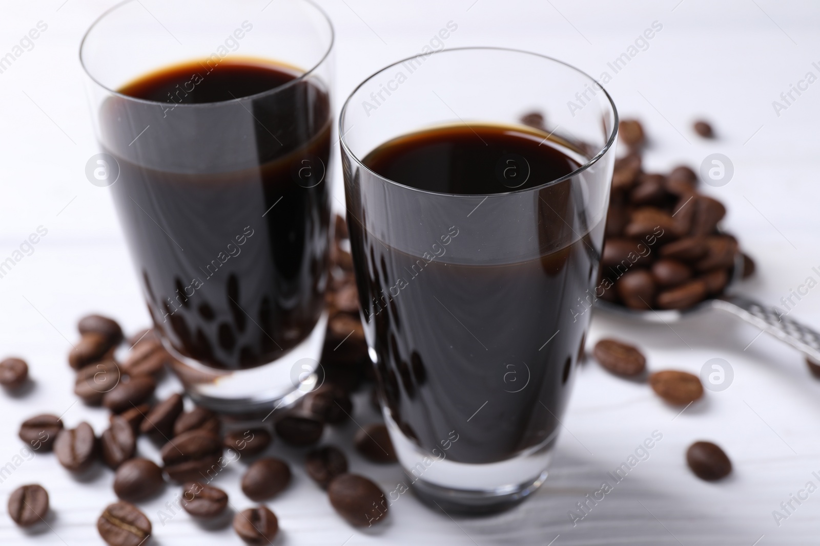 Photo of Shot glasses of coffee liqueur and beans on white table, closeup
