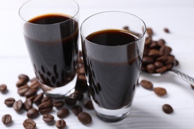 Photo of Shot glasses of coffee liqueur and beans on white table, closeup