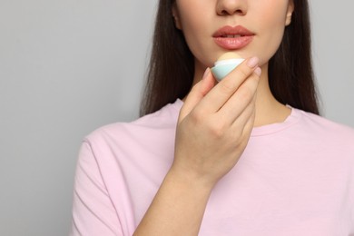 Photo of Young woman applying lip balm on grey background, closeup. Space for text