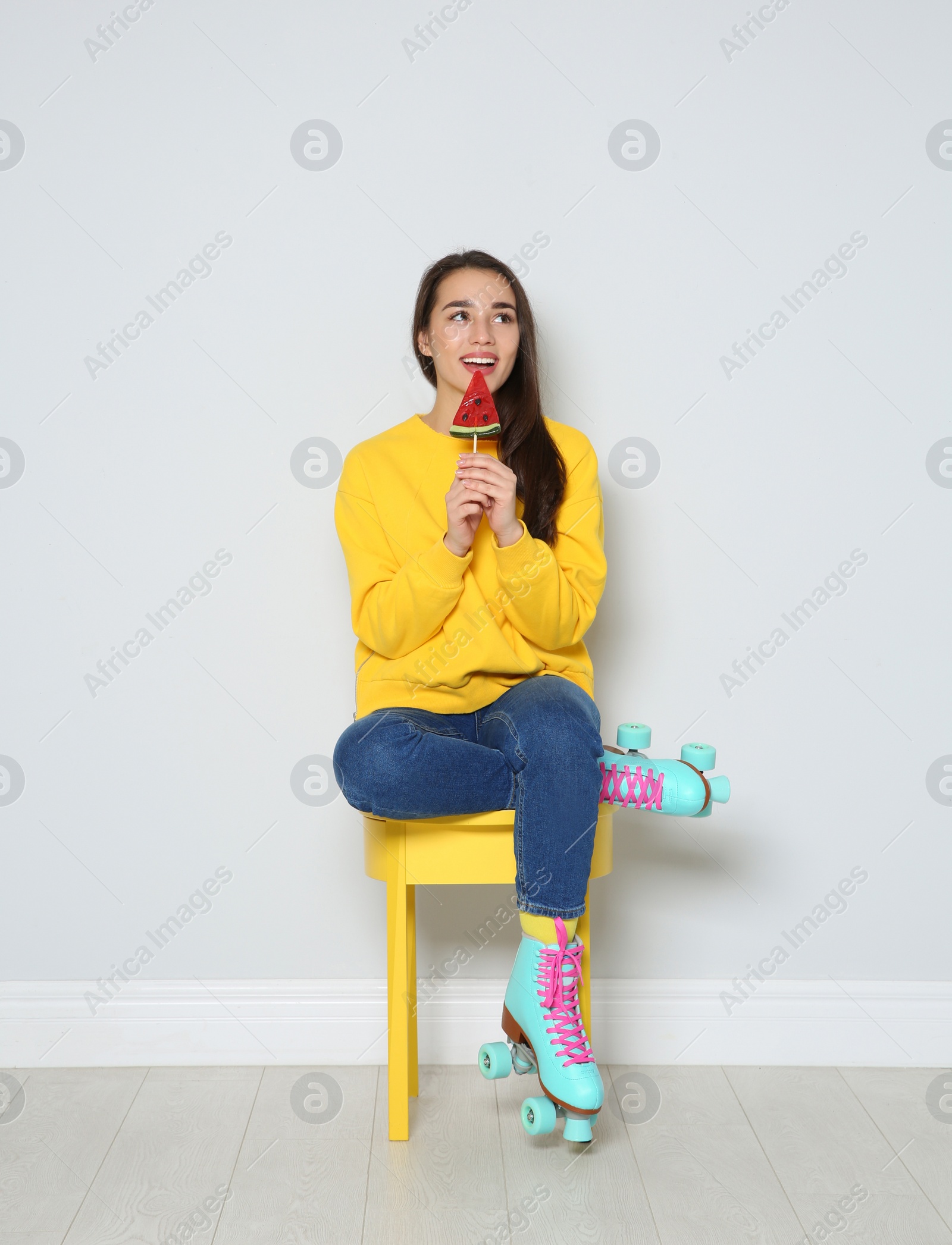 Photo of Young woman with roller skates and lollipop sitting on chair near color wall