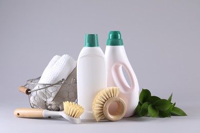 Photo of Bottles of cleaning product, brushes, rags and floral decor on light background