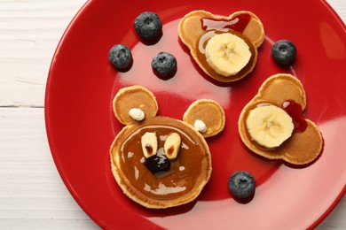 Photo of Creative serving for kids. Plate with cute bears made of pancakes, berries, banana and chocolate paste on white wooden table, top view