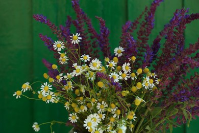 Photo of Beautiful bouquet with field flowers near green wooden wall, closeup
